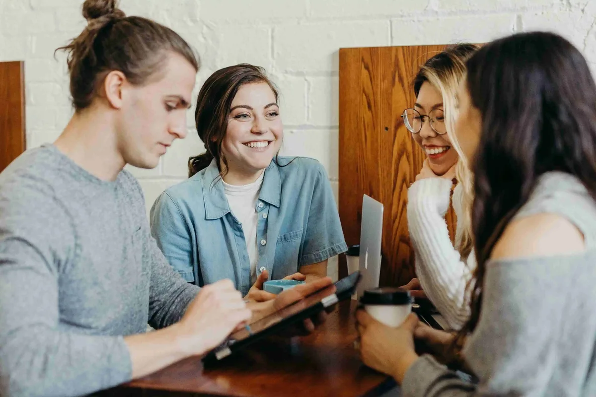 A small group sitting together at a table, talking and looking at a laptop